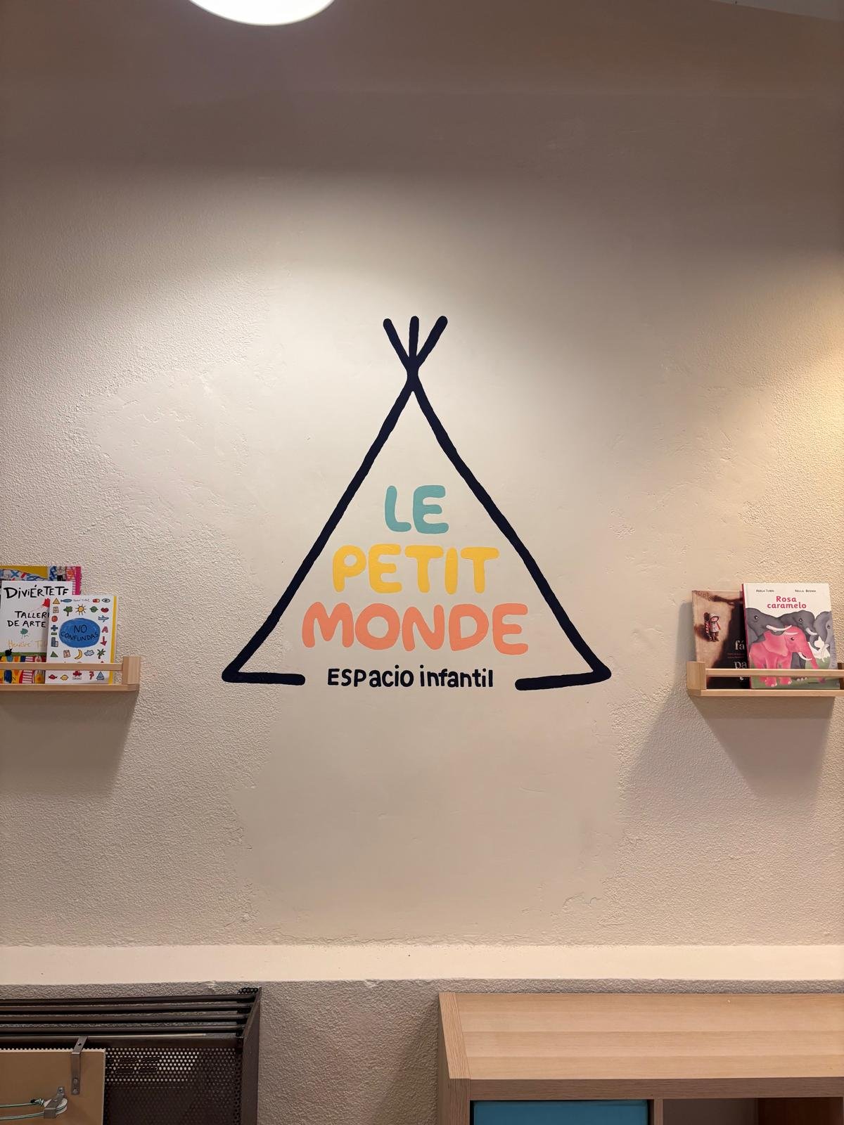 Logo de Le Petit Monde pintado en la pared con estanterías de cuentos
