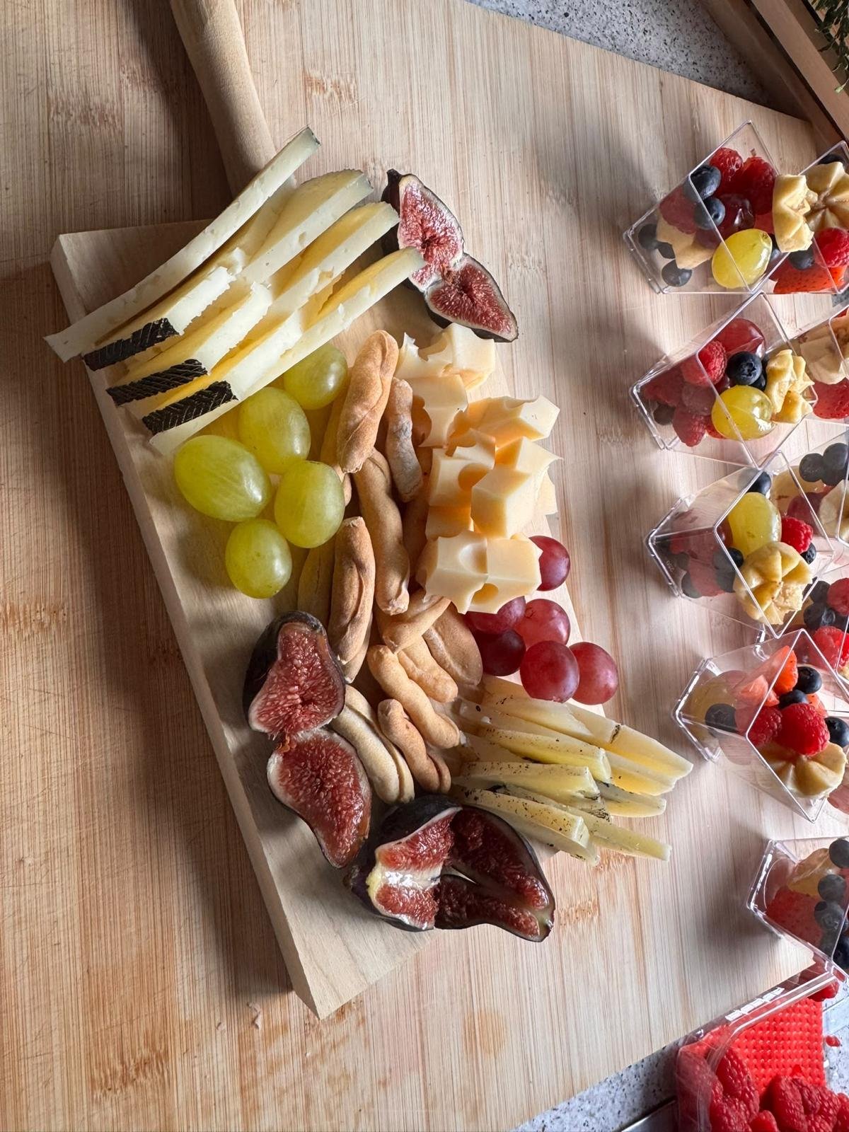 Tabla de quesos, higos y uvas con vasitos de fruta