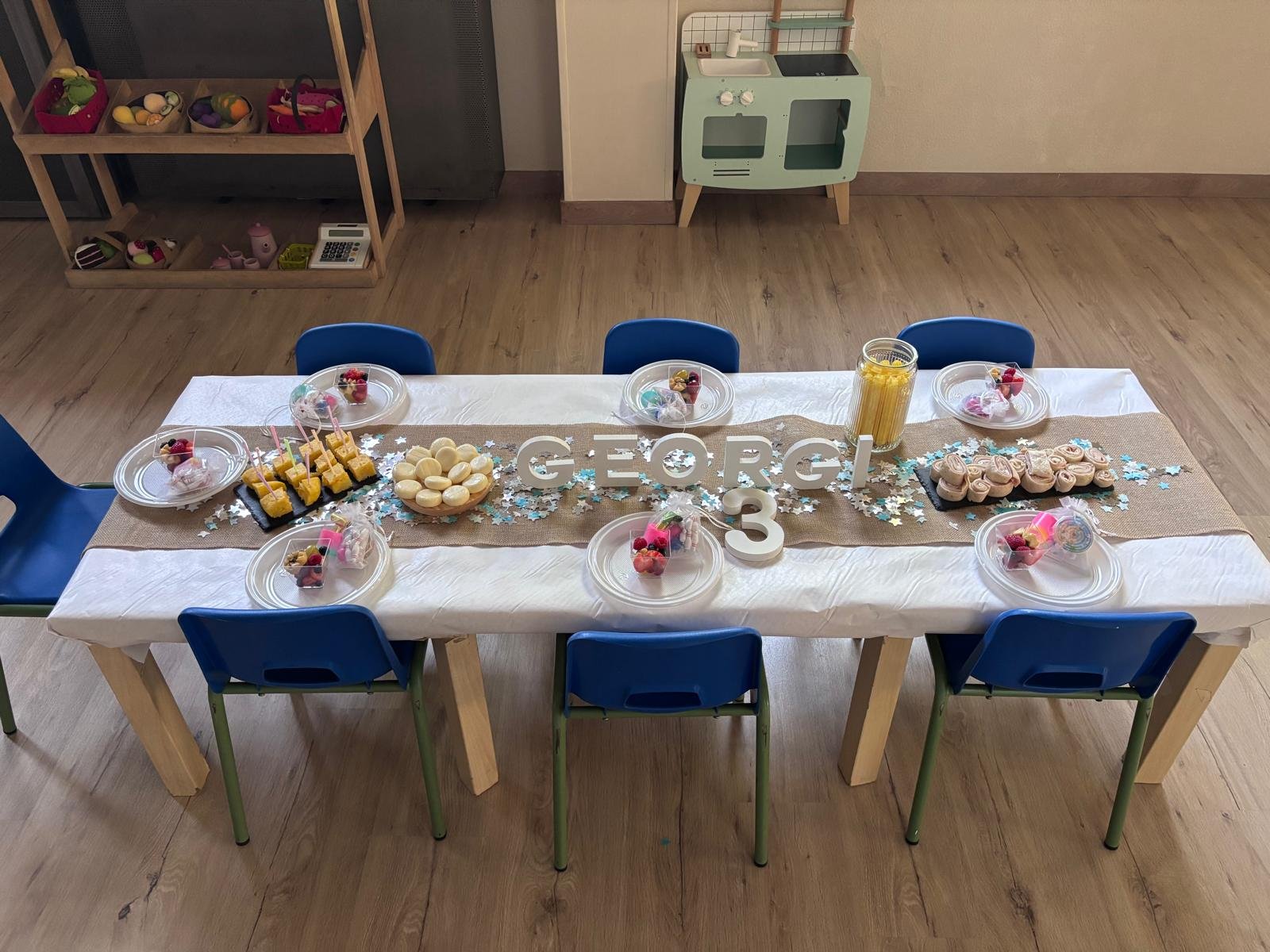 Mesa infantil decorada con sillas azules y picoteo para los peques